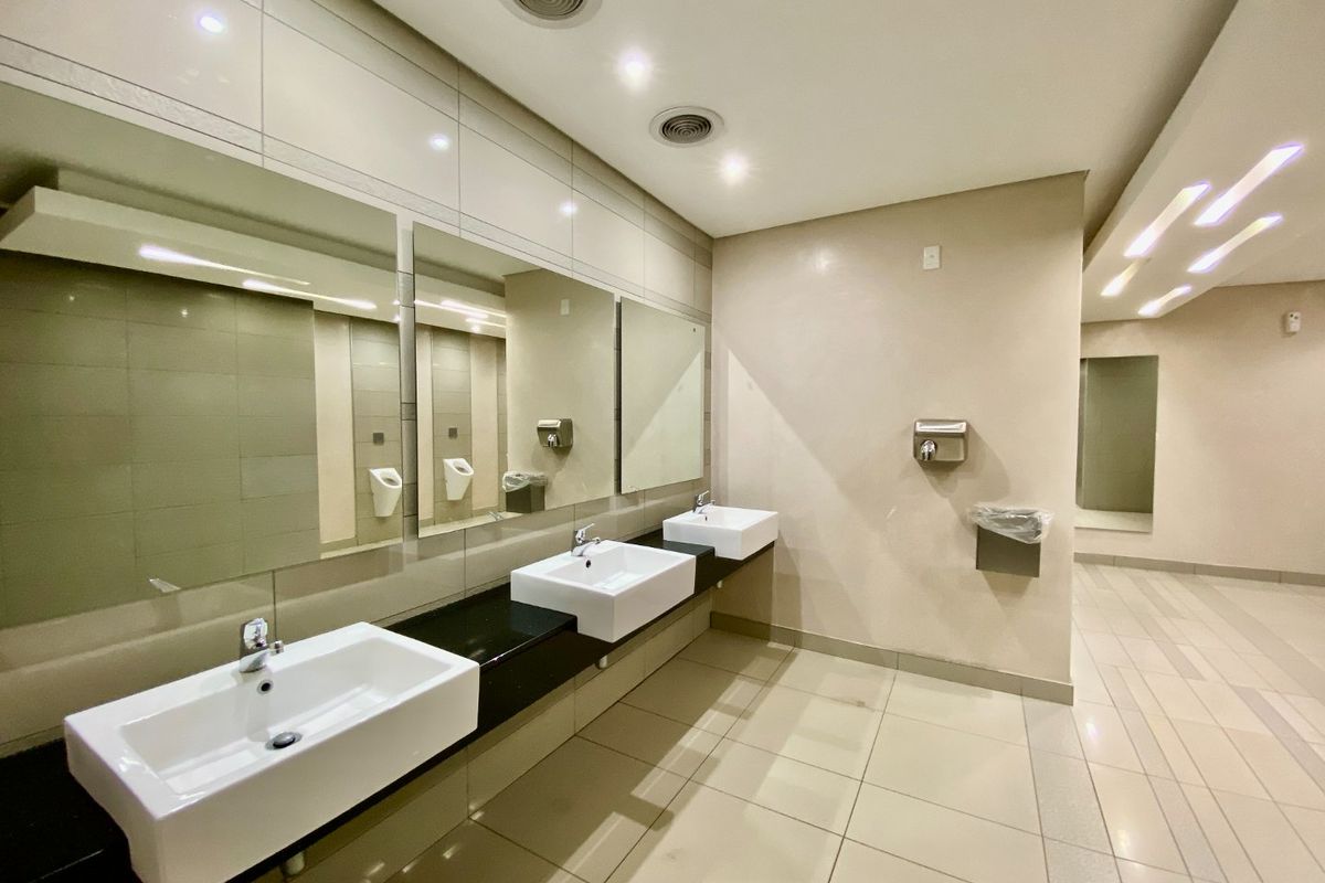 Modern commercial bathroom featuring multiple wall-mounted ceramic basins, granite vanity countertops, large mirrors, and high-quality tiled finishes with recessed lighting.