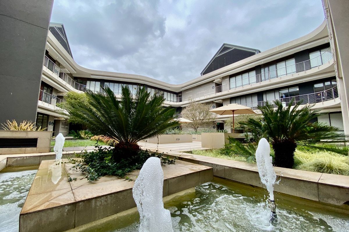 A well-maintained commercial courtyard featuring a central water fountain, stone paving, and landscaped garden beds surrounded by a multi-story office building.