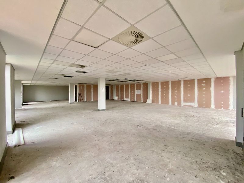 A large, open-plan commercial office space featuring a suspended ceiling, structural columns, and unfinished drywall partitions, ready for custom fit-out.