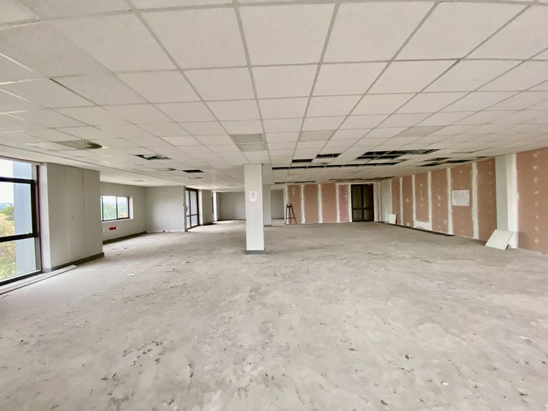 An expansive, open-plan commercial office space currently in a shell condition with unfinished walls, exposed ceiling grid, and concrete flooring.