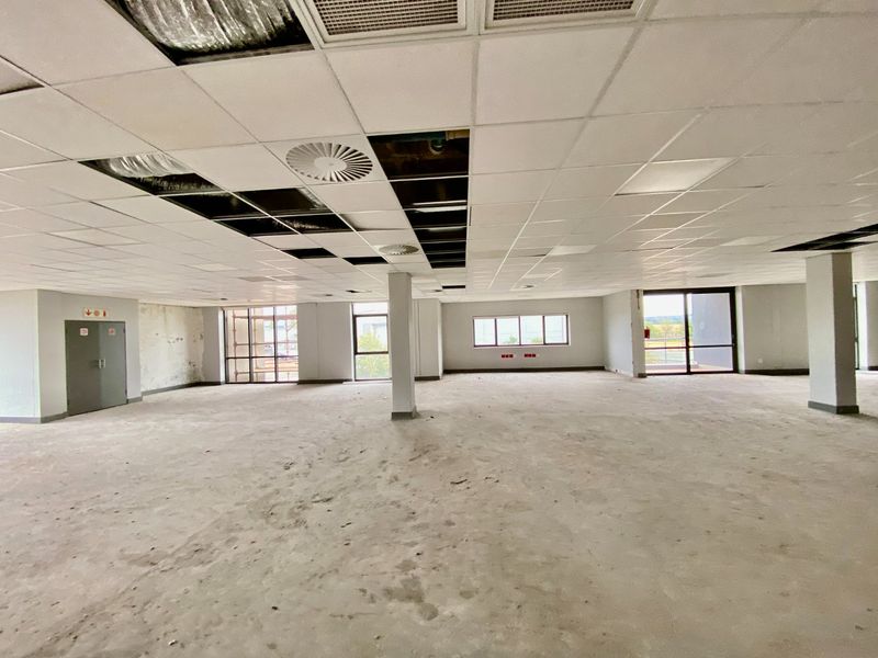 Expansive open-plan commercial office space featuring large windows, structural columns, and a suspended ceiling requiring repair and flooring completion.