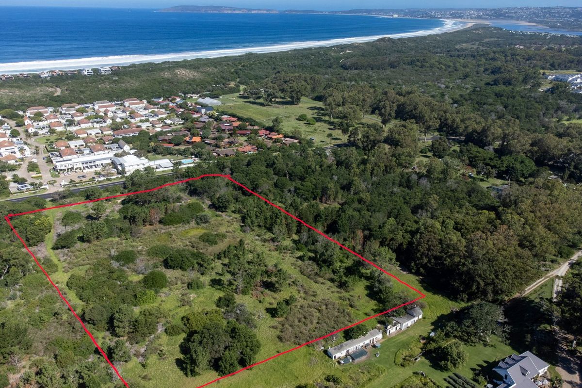 An aerial view of a vacant residential plot featuring coastal vegetation, with the coastline and surrounding neighborhood visible in the background.