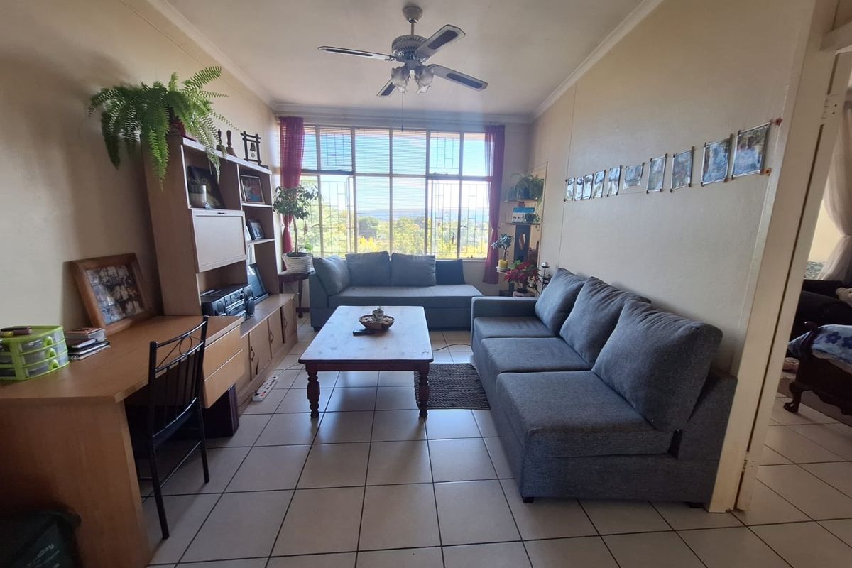 A living room featuring tiled flooring, a ceiling fan, and a large window with security bars providing natural light.