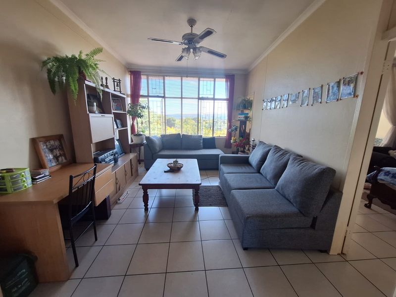 A living room featuring tiled flooring, a ceiling fan, and a large window with security bars providing natural light.