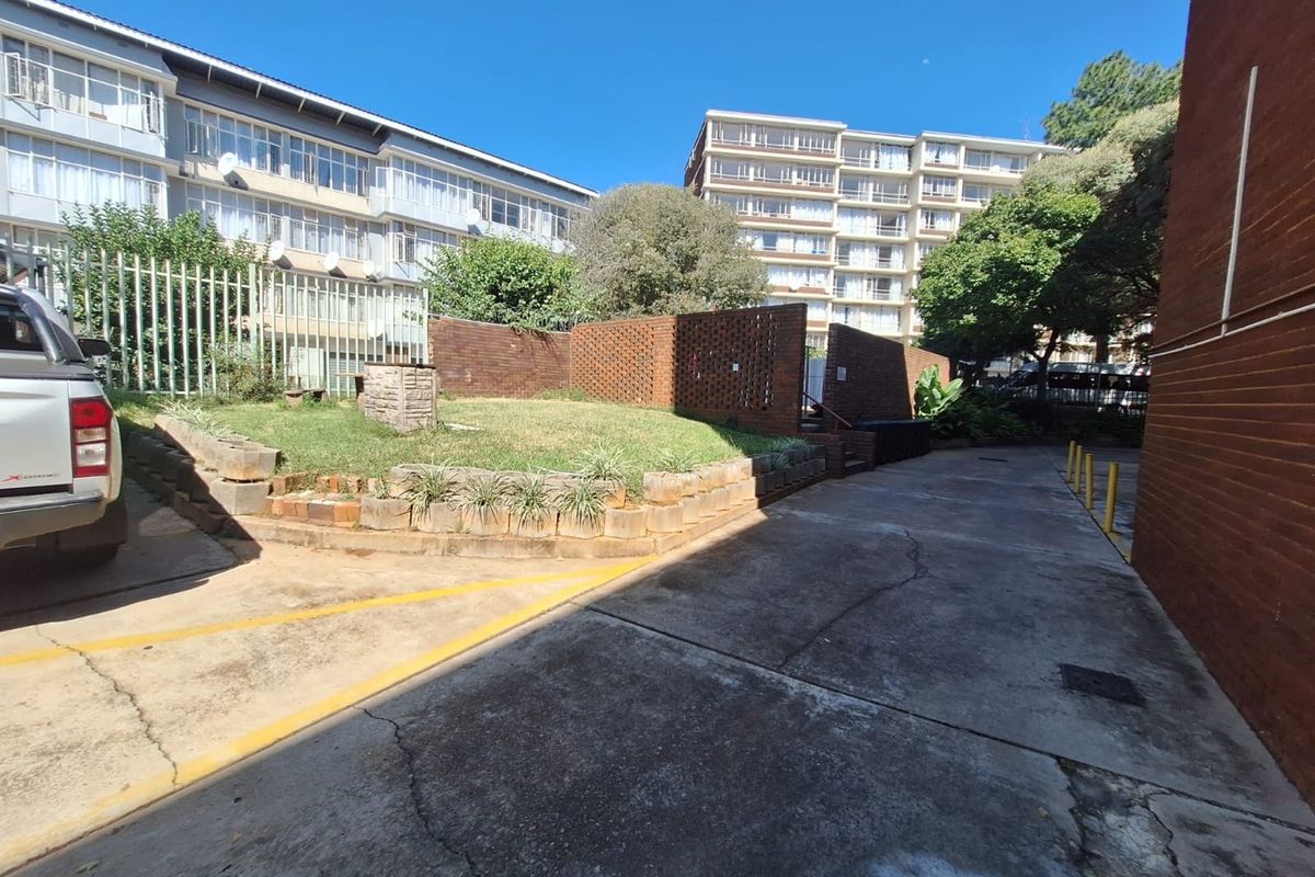Exterior view of the apartment complex rear area featuring a concrete driveway, brick retaining walls, and landscaped garden beds.