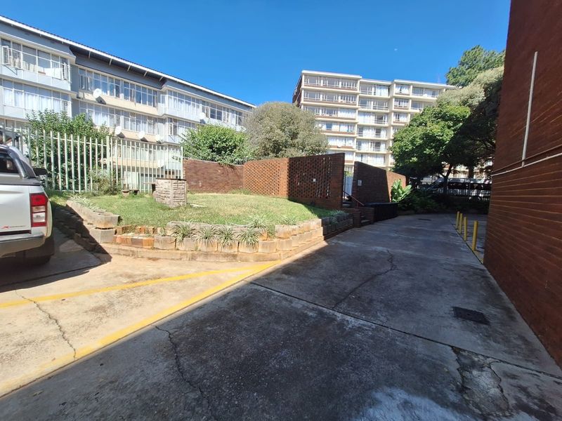 Exterior view of the apartment complex rear area featuring a concrete driveway, brick retaining walls, and landscaped garden beds.