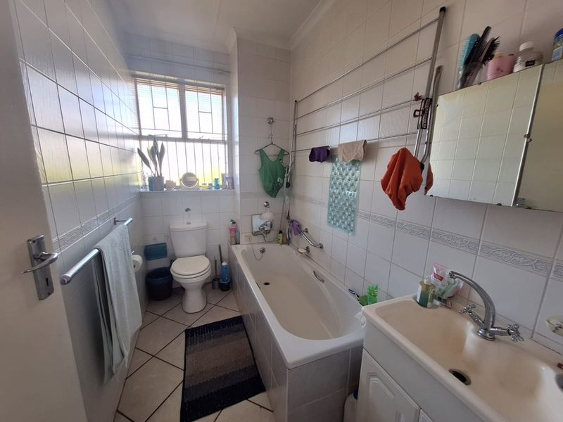 A functional bathroom featuring a built-in bathtub, toilet, and vanity basin with tiled walls and flooring, offering a classic layout.