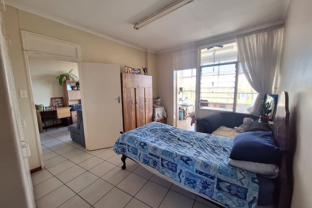 A bedroom featuring tiled flooring, a built-in wardrobe, and a large window providing natural light, with access to an adjoining room.