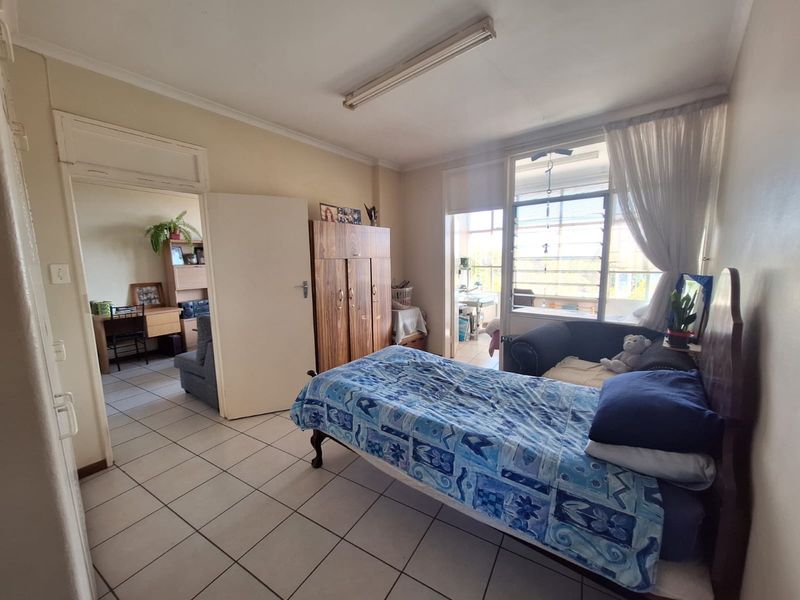 A bedroom featuring tiled flooring, a built-in wardrobe, and a large window providing natural light, with access to an adjoining room.