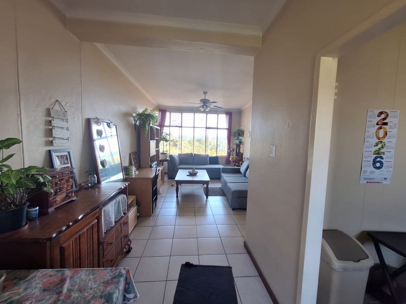A spacious living room featuring tiled flooring, a ceiling fan, and a large window providing natural light and an exterior view.