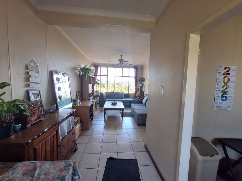 An open-plan living area featuring tiled flooring, a ceiling fan, and a large window providing natural light and views.