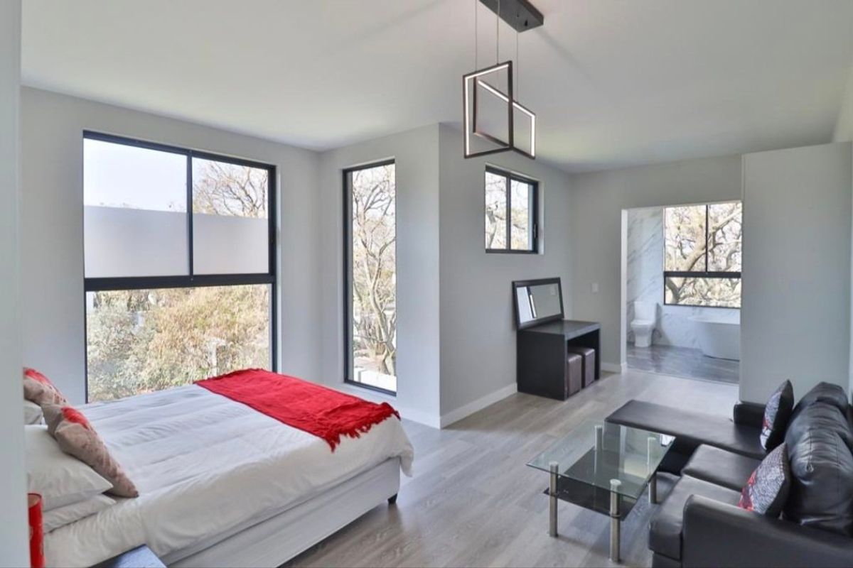 Spacious modern bedroom featuring laminate flooring, large black-framed windows with natural light, and an open-plan en-suite bathroom.