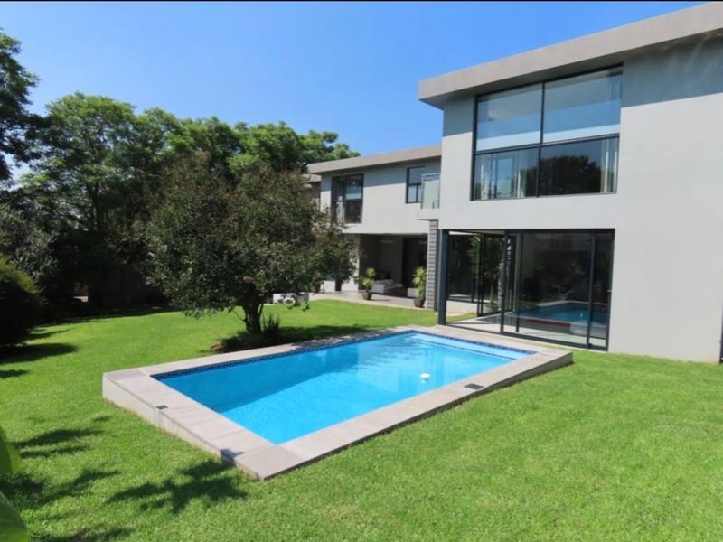 A modern double-storey home featuring a well-maintained swimming pool, expansive lawn, and large glass sliding doors opening to the outdoor area.