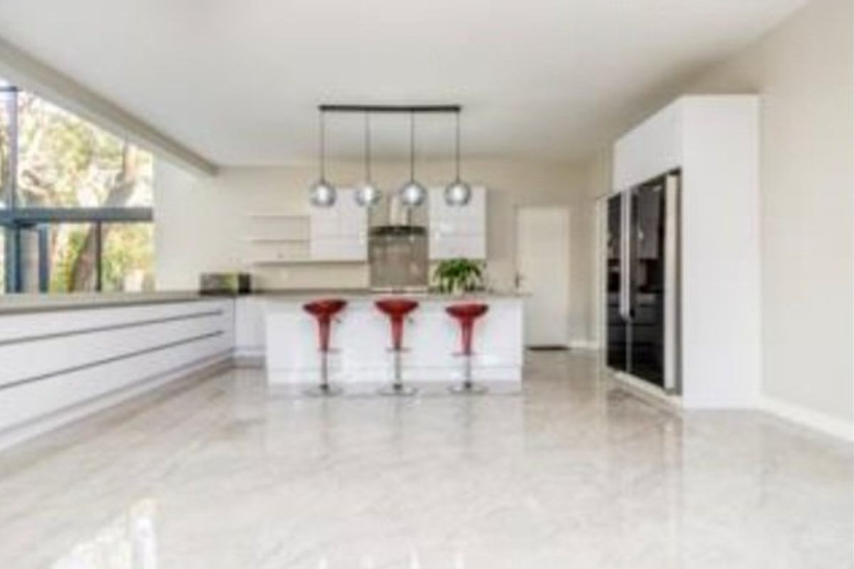 Modern open-plan kitchen featuring a central island, sleek white cabinetry, integrated appliances, and polished tiled flooring with large windows providing natural light.