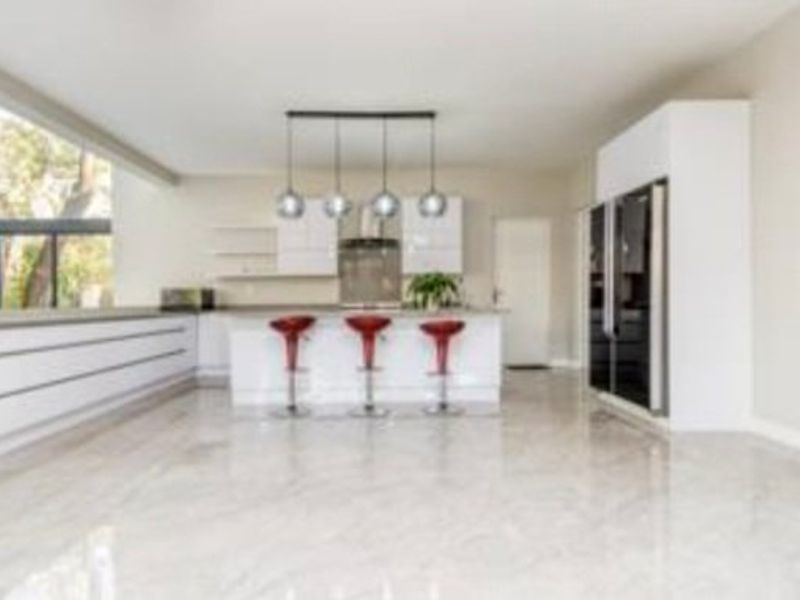 Modern open-plan kitchen featuring a central island, sleek white cabinetry, integrated appliances, and polished tiled flooring with large windows providing natural light.