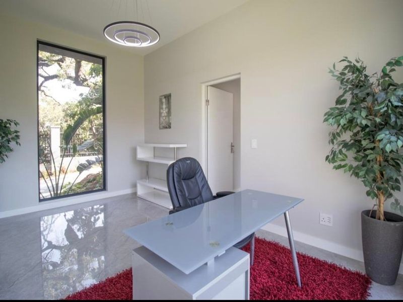 A bright and modern home office featuring polished floor tiles, a large window with garden views, and contemporary lighting.