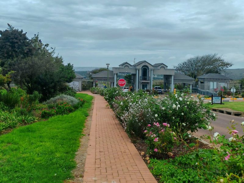 A well-maintained paved walkway leading towards the gated entrance of a residential estate, surrounded by lush landscaped gardens.