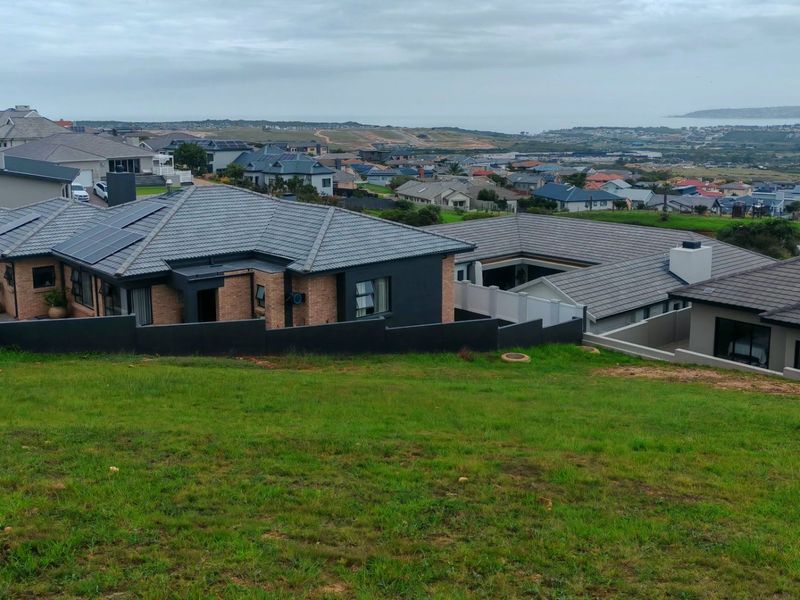 An elevated view overlooking a residential neighborhood with a sloped grassy foreground and distant coastal landscape.
