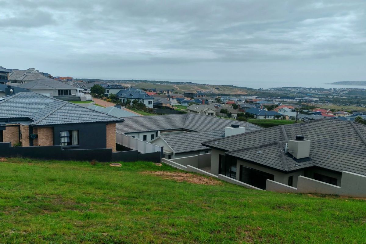 An elevated view overlooking a residential neighborhood with a sloped grass foreground and distant coastal landscape.
