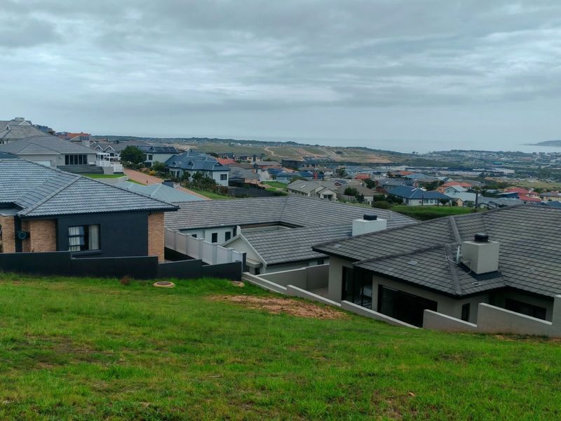 An elevated view overlooking a residential neighborhood with a sloped grass foreground and distant coastal landscape.
