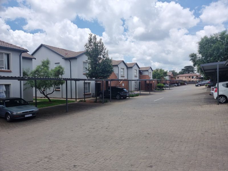 A view of the townhouse complex exterior featuring paved driveways and covered carport parking bays for residents.