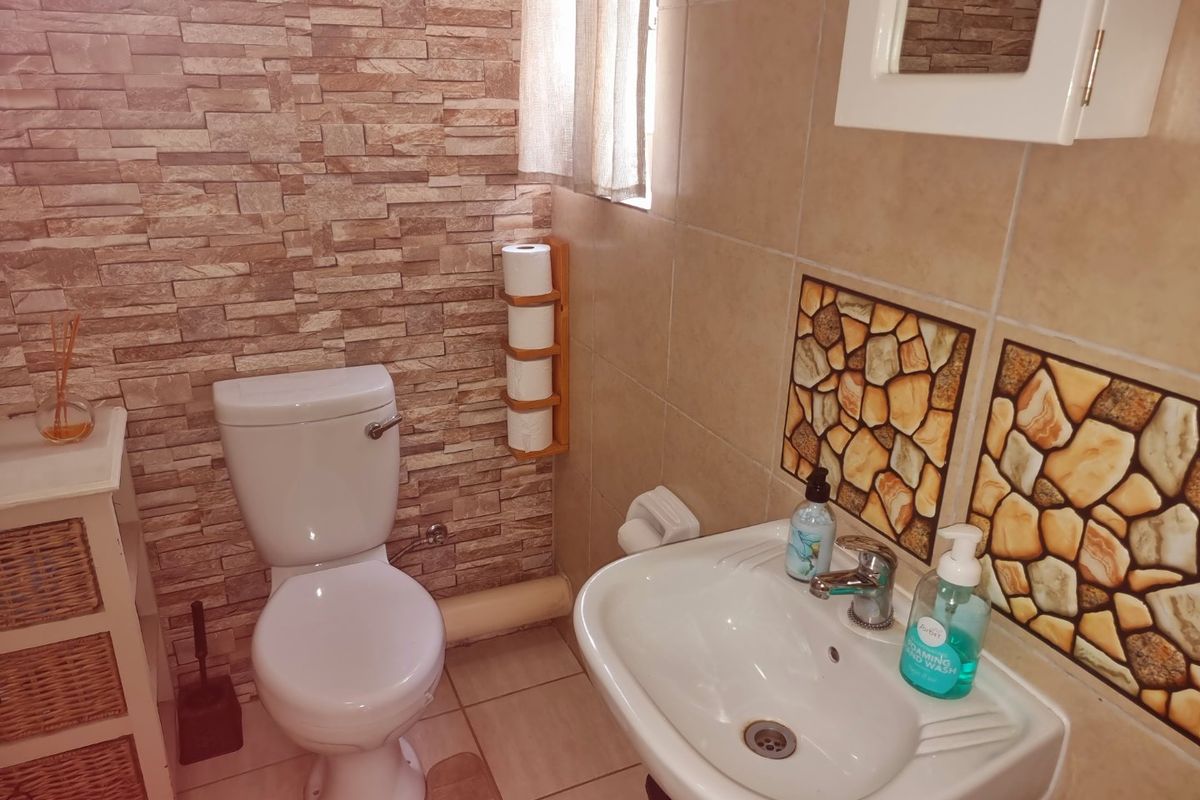 A compact bathroom featuring stone-effect wall cladding, ceramic floor tiles, a pedestal washbasin, and a standard toilet.