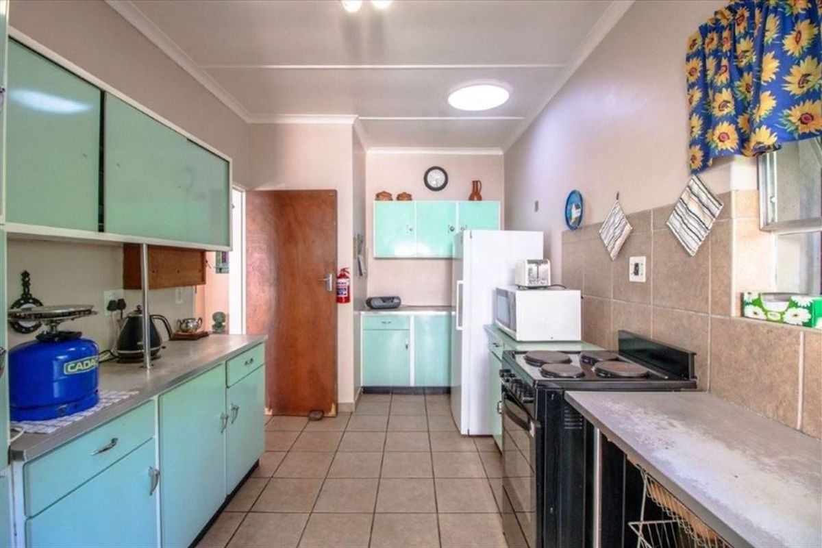 A functional kitchen featuring vintage-style cabinetry, tiled flooring, a tiled backsplash, and a freestanding stove, offering potential for a modern renovation.