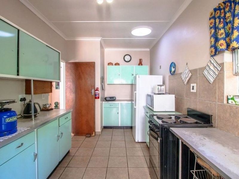 A functional kitchen featuring vintage-style cabinetry, tiled flooring, a tiled backsplash, and a freestanding stove, offering potential for a modern renovation.