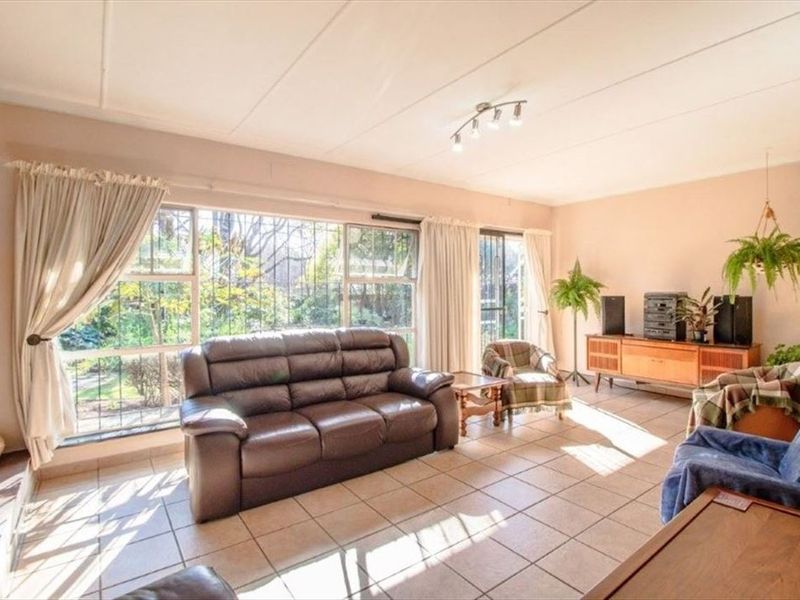 A spacious living room featuring large windows with security bars, tiled flooring, and neutral wall finishes, offering plenty of natural light.