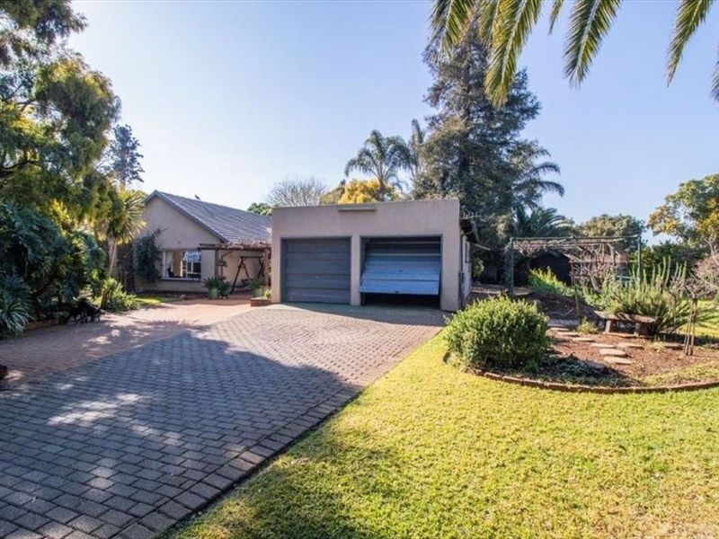 Front view of the property featuring a paved driveway, established garden, and a double garage with one damaged door.