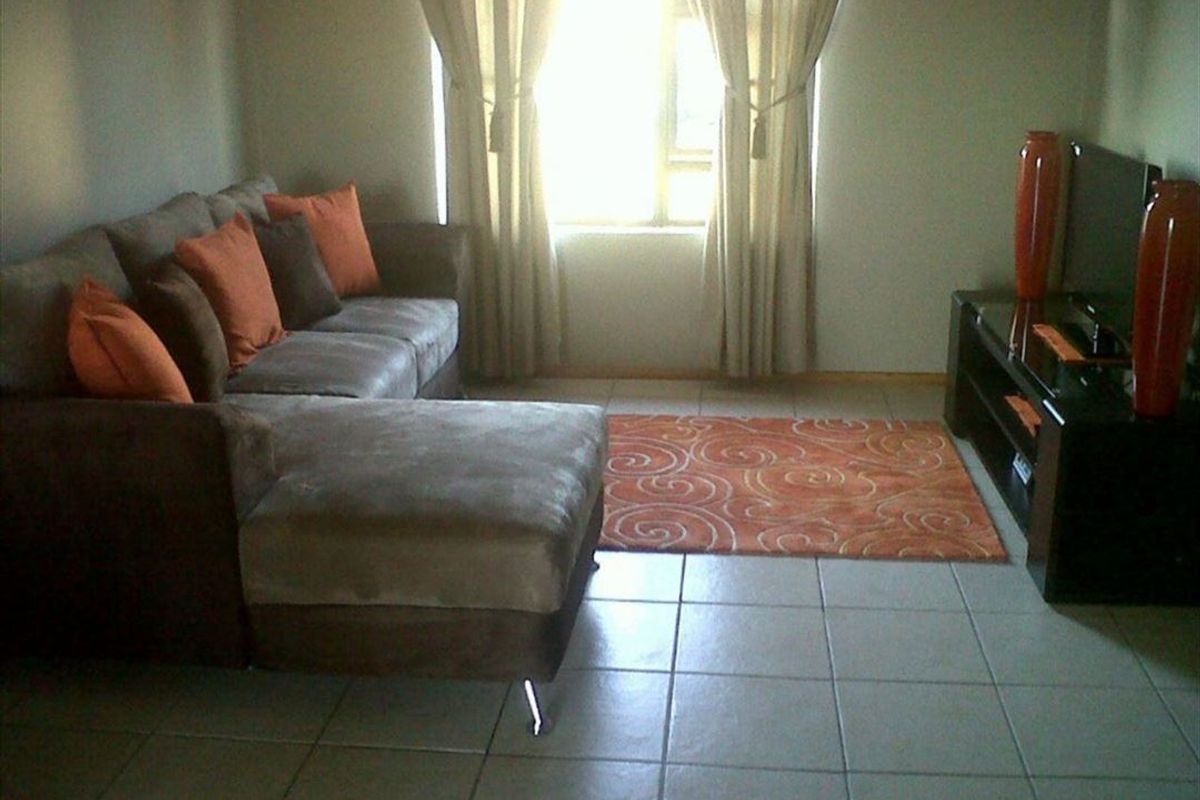 A living room area featuring neutral tiled flooring and a window with installed curtain rails.