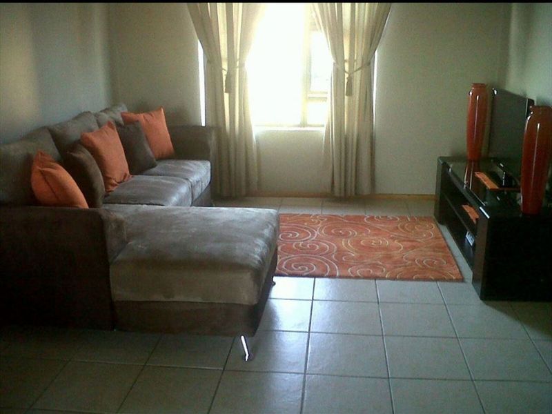 A living room area featuring neutral tiled flooring and a window with installed curtain rails.