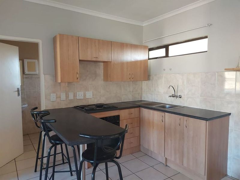A functional kitchen featuring laminate cabinetry, dark countertops, a built-in hob and oven, and tiled flooring with a breakfast bar area.