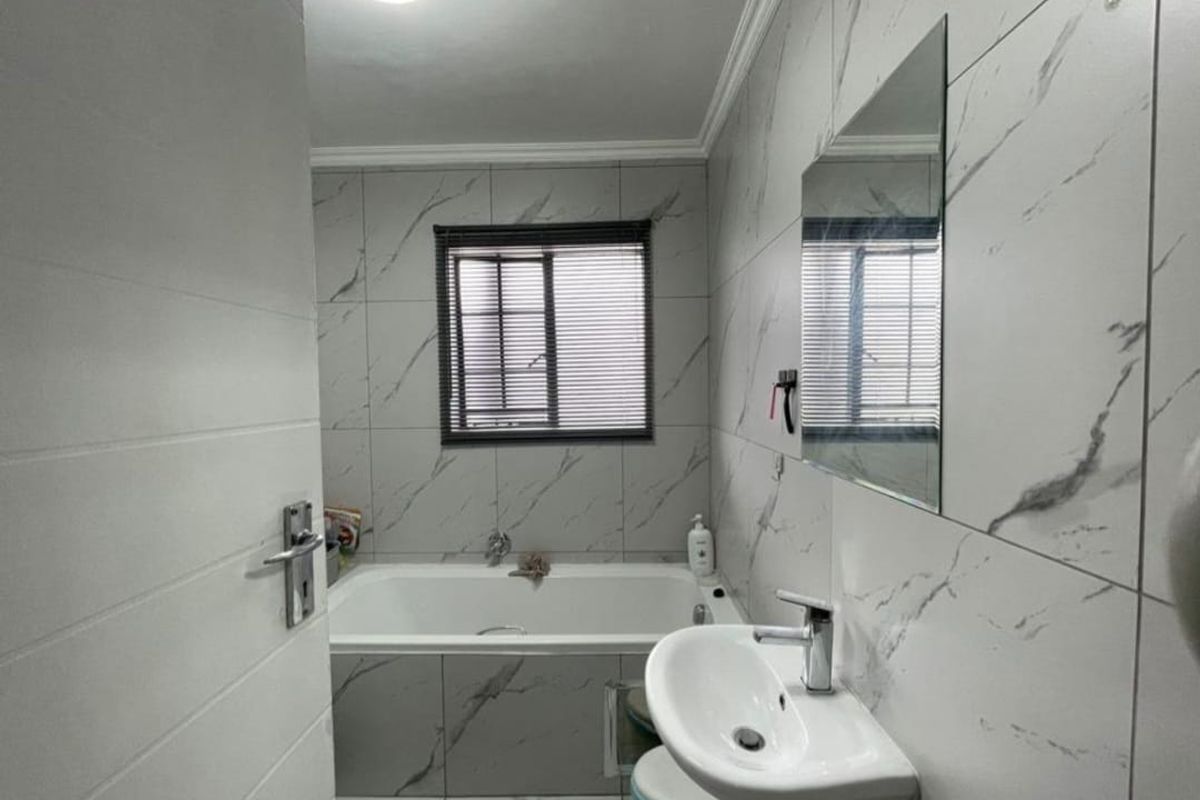 Modern bathroom featuring marble-look wall tiles, a pedestal basin, and a built-in bathtub with a window providing natural light.