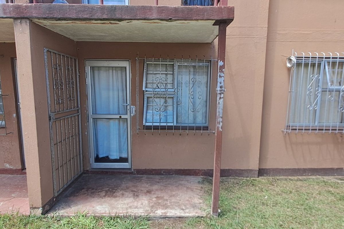 Ground floor apartment exterior featuring a concrete patio, security gates, and protective window bars on a weathered brown facade.