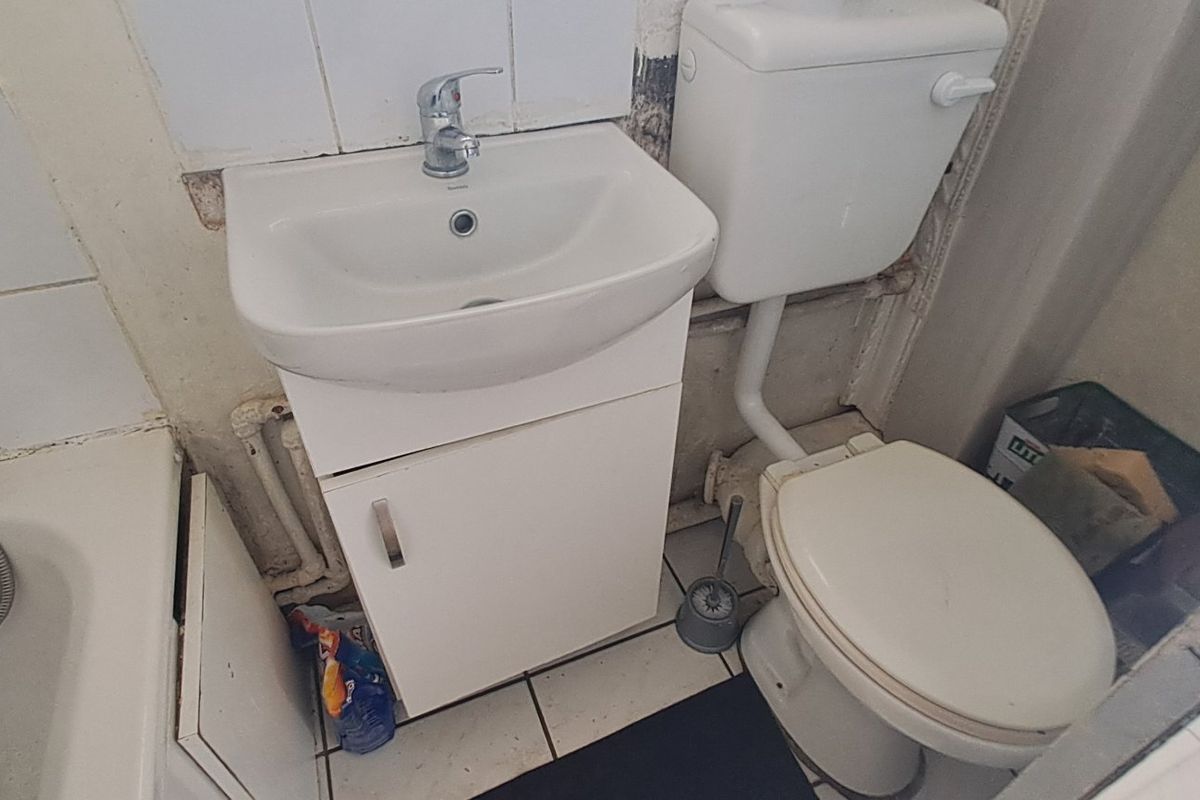 Compact bathroom featuring a standard bathtub, pedestal basin, and toilet, requiring significant cosmetic updates and repairs to wall finishes and fixtures.