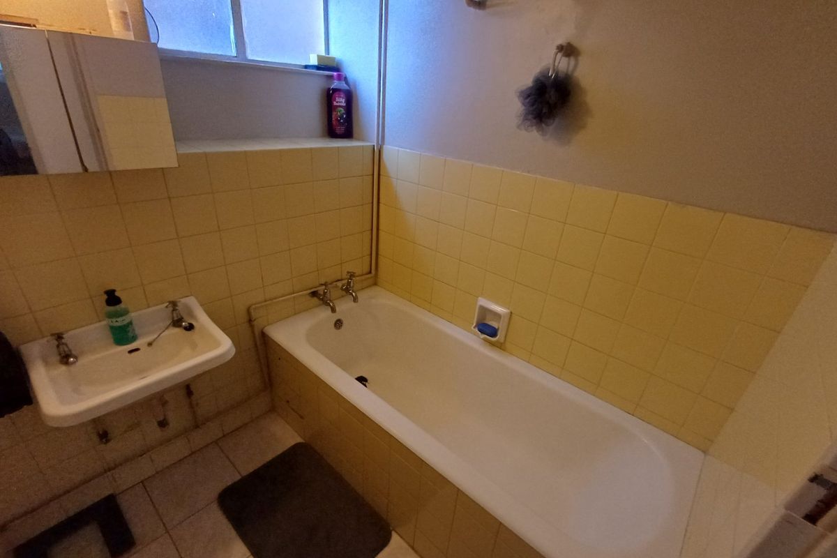 A dated bathroom featuring a wall-mounted basin, a standard bathtub, and yellow ceramic wall tiling with exposed plumbing fixtures.