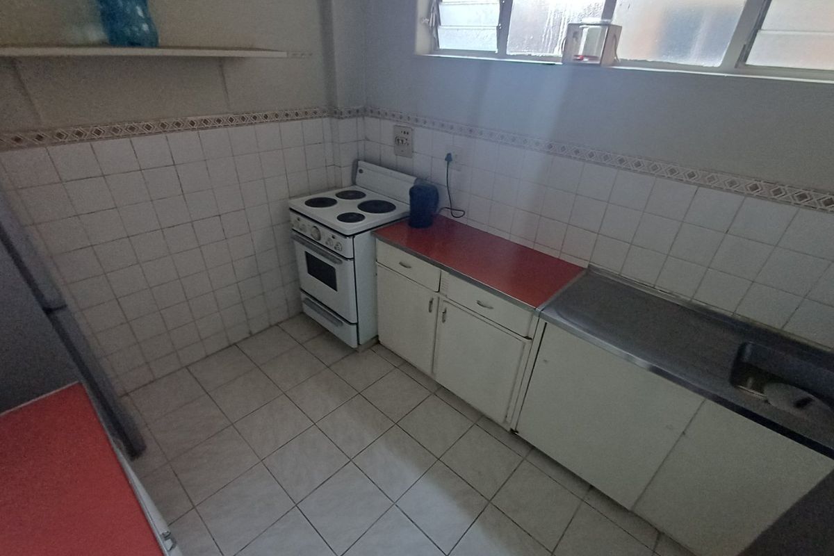 A functional kitchen featuring tiled splashbacks, built-in cabinetry, a stainless steel sink, and an electric stove, offering potential for modernization.