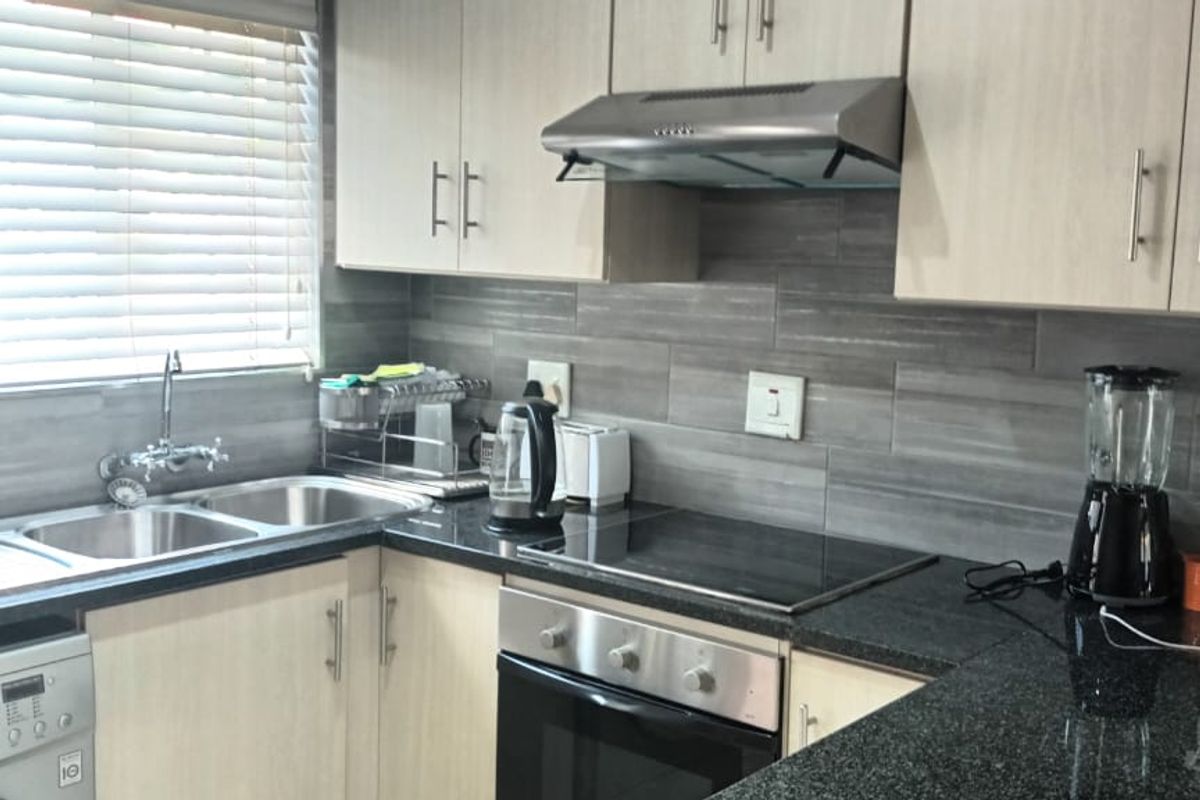 Modern kitchen featuring light wood cabinetry, granite countertops, a double sink, built-in oven, electric hob, and a tiled backsplash.