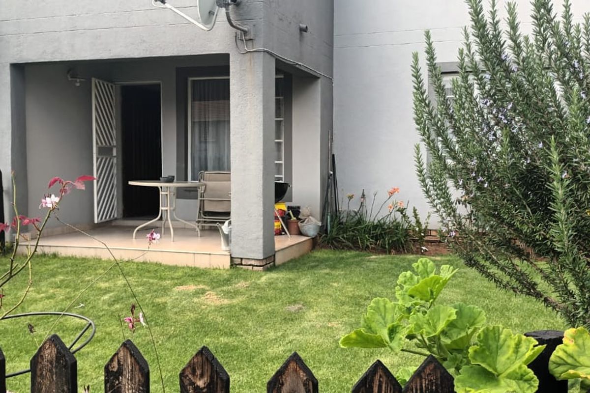 A rear view of the townhouse featuring a covered patio with tiled flooring, a small private lawn, and a picket fence boundary.