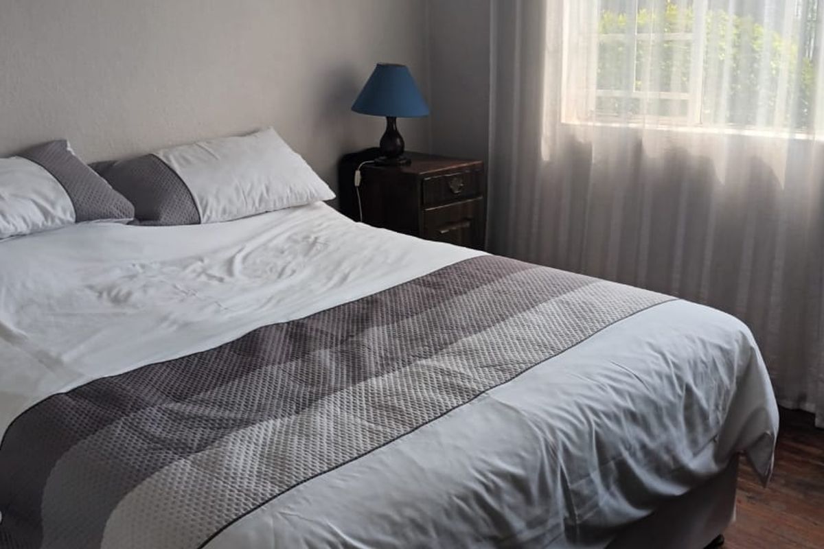 A bedroom featuring laminate flooring and a window with security bars, providing natural light and a view of the exterior greenery.