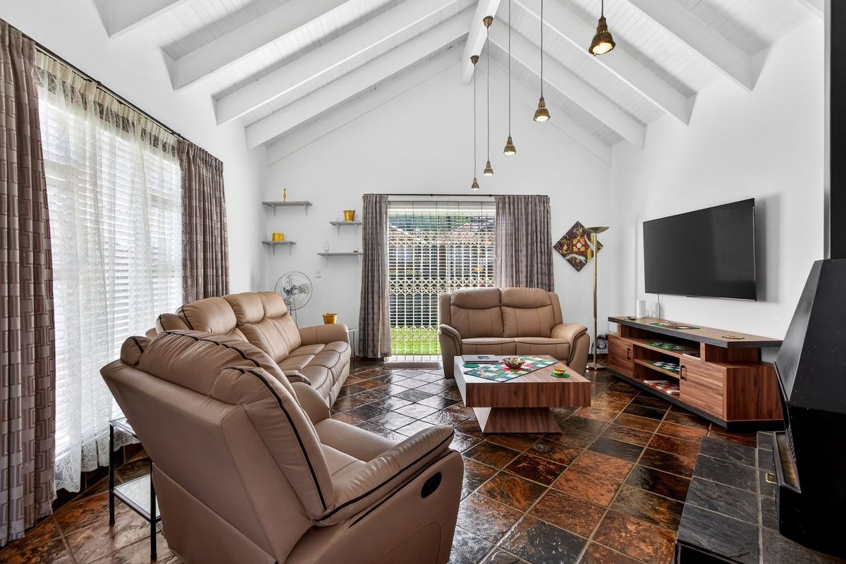 Spacious living room featuring a high vaulted ceiling with exposed beams, tiled flooring, and a built-in fireplace, offering access to the rear garden.