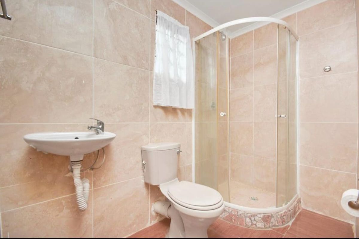 A functional bathroom featuring a corner shower enclosure, wall-mounted basin, and toilet with neutral wall tiling throughout.