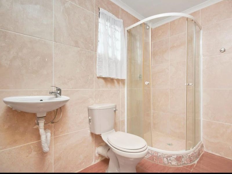 A functional bathroom featuring a corner shower enclosure, wall-mounted basin, and toilet with neutral wall tiling throughout.