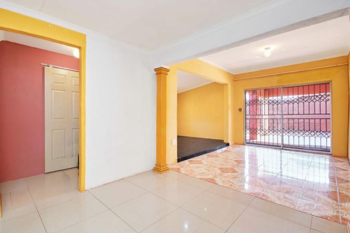 An empty living area featuring tiled flooring, a decorative column, and a sliding glass door with a security gate leading to the exterior.