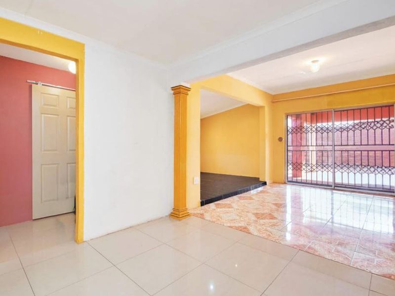An empty living area featuring tiled flooring, a decorative column, and a sliding glass door with a security gate leading to the exterior.