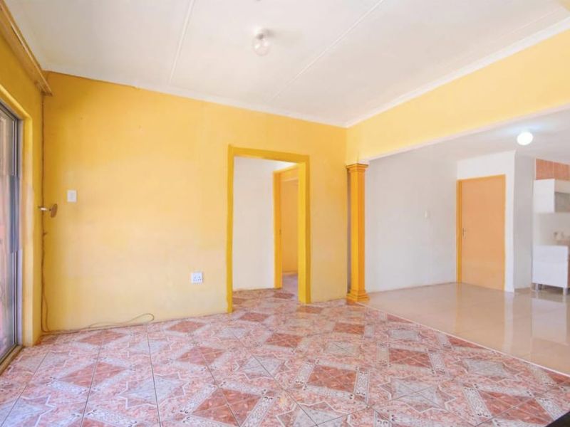 An empty open-plan living area featuring tiled flooring, decorative columns, and a sliding glass door with a security gate leading to the exterior.