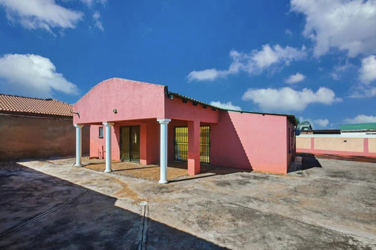 Rear view of the property featuring a covered patio area with concrete columns and a large paved courtyard.