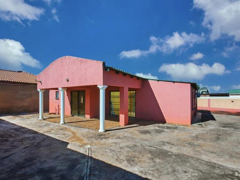 Rear view of the property featuring a covered patio area with concrete columns and a large paved courtyard.