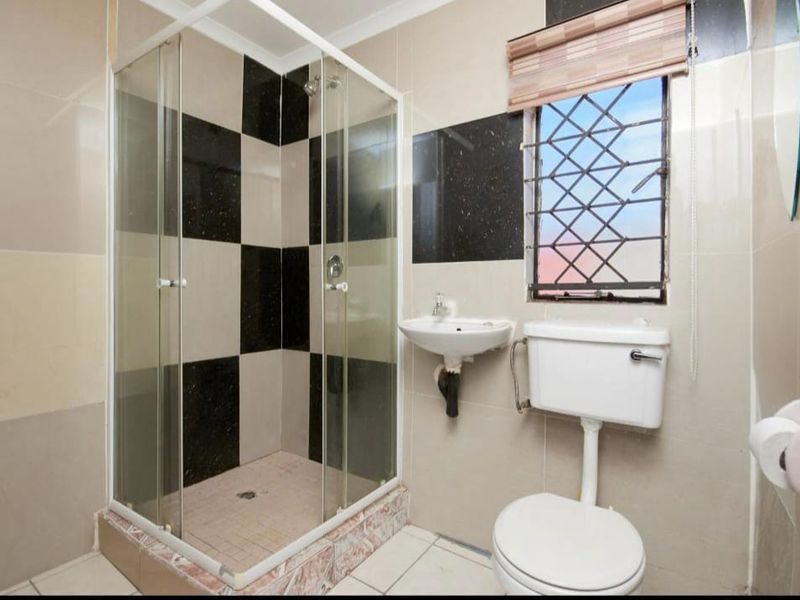 A functional bathroom featuring a shower enclosure, wall-mounted basin, and toilet with a checkerboard tiled wall finish.